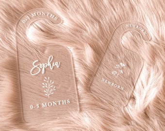 May include: Two clear acrylic hangers with white text and a floral design. The larger hanger says "Sophia" and "0-3 Months". The smaller hanger says "Newborn".
