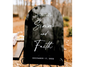 May include: Black welcome sign with white text that reads "Welcome to the wedding of Simon and Faith, December 17, 2022".