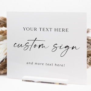 May include: A white custom sign with black text that reads "YOUR TEXT HERE", "custom sign", and "and more text here!". The sign is held by a clear acrylic stand.