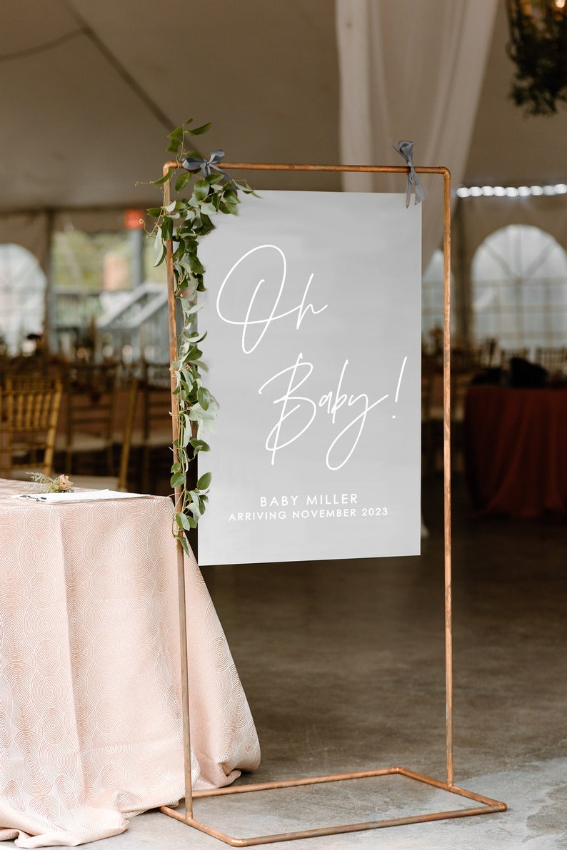 Peut inclure: Une pancarte blanche avec le texte "Oh Baby!" en &eacute;criture cursive. Sous le texte, on peut lire "Baby Miller Arriving November 2023". La pancarte est sur un support en cuivre avec de la verdure.