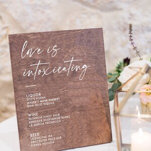 May include: A wooden sign with the text "love is intoxicating" in white script. The sign lists various liquor, wine, and beer options.
