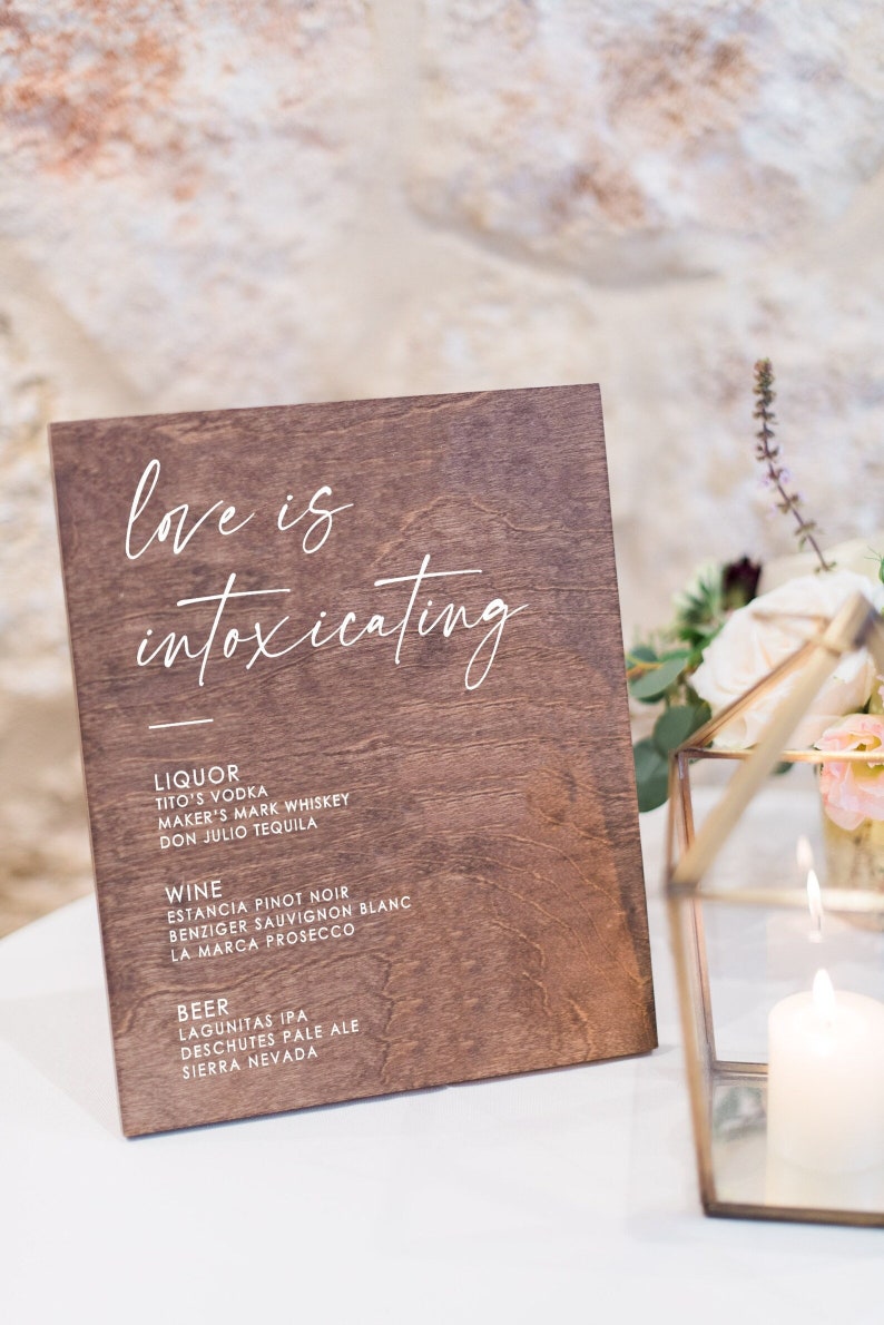 May include: A wooden sign with the text "love is intoxicating" in white script. The sign lists various liquor, wine, and beer options.