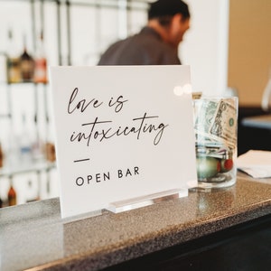 May include: White sign with black text that reads "love is intoxicating" and "OPEN BAR".