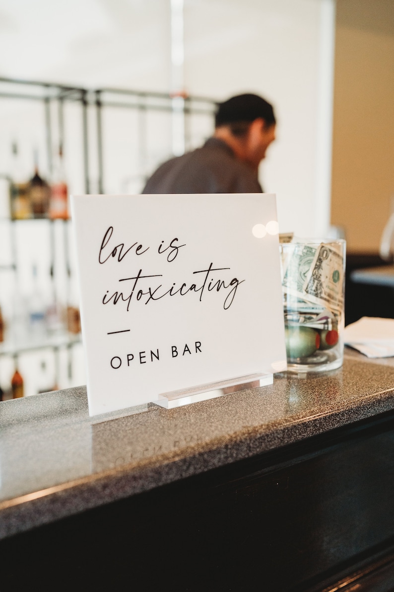 May include: White sign with black text that reads "love is intoxicating" and "OPEN BAR".