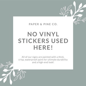 May include: A white sign with a gray background and green leafy branches on either side. The sign reads "PAPER & PINE CO. NO VINYL STICKERS USED HERE! All of our signs are painted with a thick, crisp, waterproof paint for ultimate durability and a high-end look!"