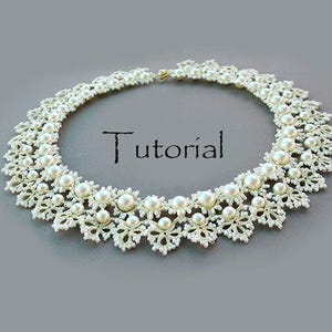 Può includere: Una collana a colletto in pizzo chiacchierino bianco con una disposizione circolare di intricati motivi a filo annodato e perle rotonde color crema incastonate. La parola Tutorial è stampata al centro in un carattere serif nero.