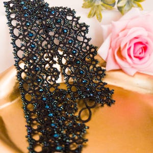 Pu&ograve; includere: Un girocollo in pizzo nero con perline blu, esposto su una superficie dorata.