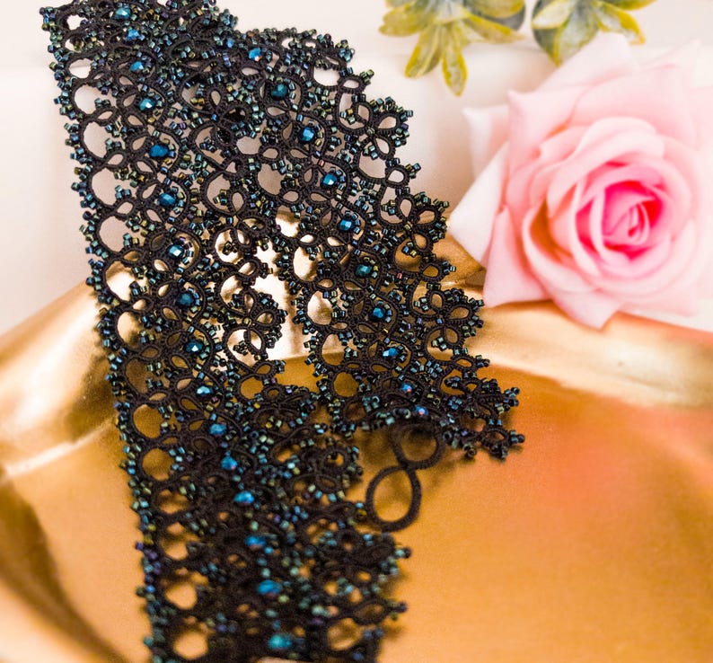 Pu&ograve; includere: Un girocollo in pizzo nero con perline blu, esposto su una superficie dorata.