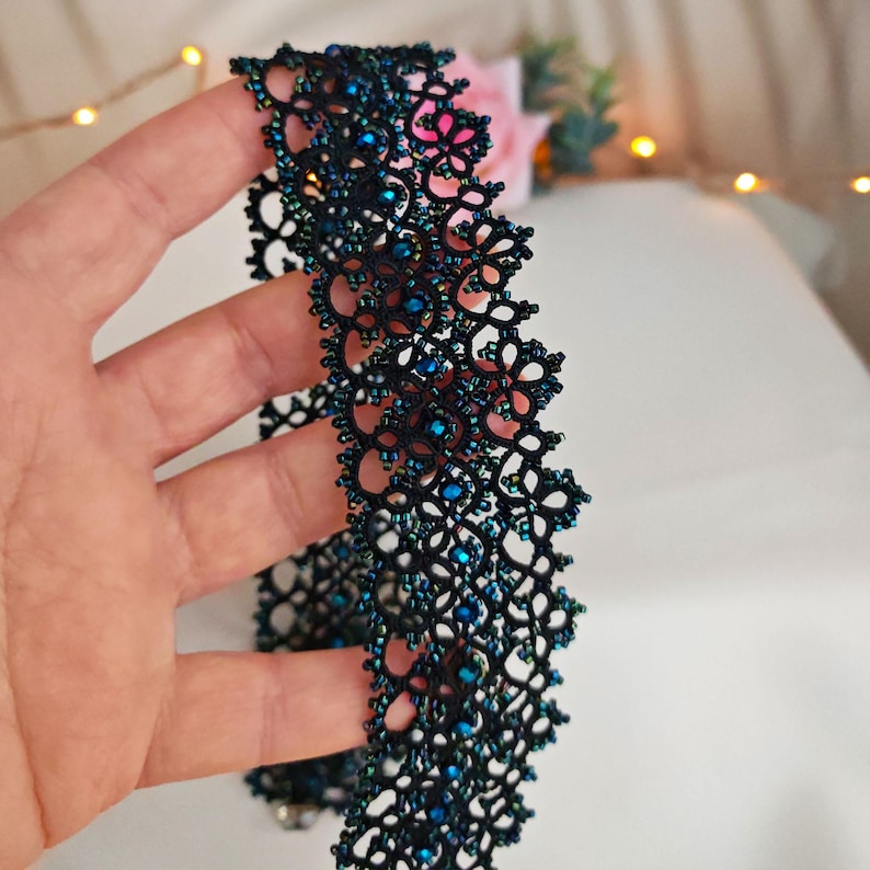 Pu&ograve; includere: Un girocollo in pizzo nero e blu con perline. Il girocollo &egrave; realizzato in pizzo delicato e intricato con piccole perline blu iridescenti.