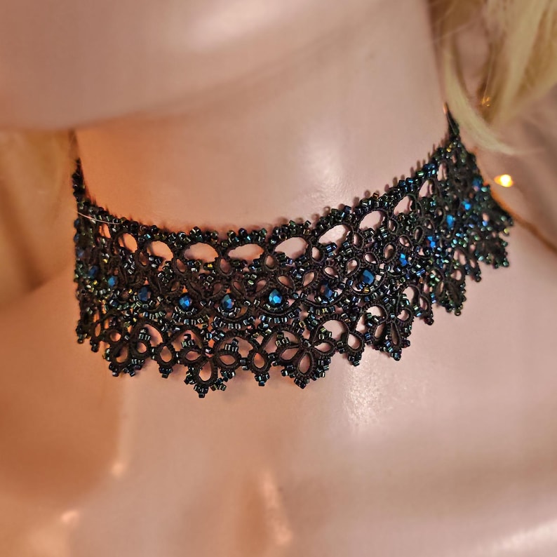 Pu&ograve; includere: Un girocollo in pizzo nero con perline blu iridescenti. Il girocollo &egrave; delicato e intricato, con un bordo a festoni.