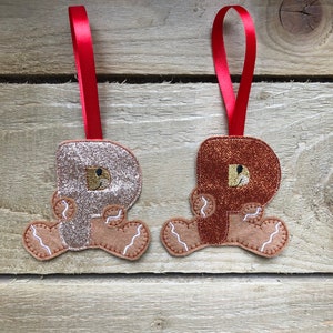 May include: Two gingerbread man ornaments with red ribbon hangers. One is gold glitter and the other is brown glitter.