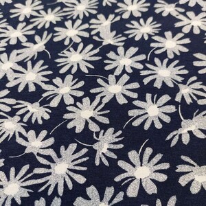 May include: A navy blue fabric with a white floral pattern. The fabric is covered in white daisy-like flowers.