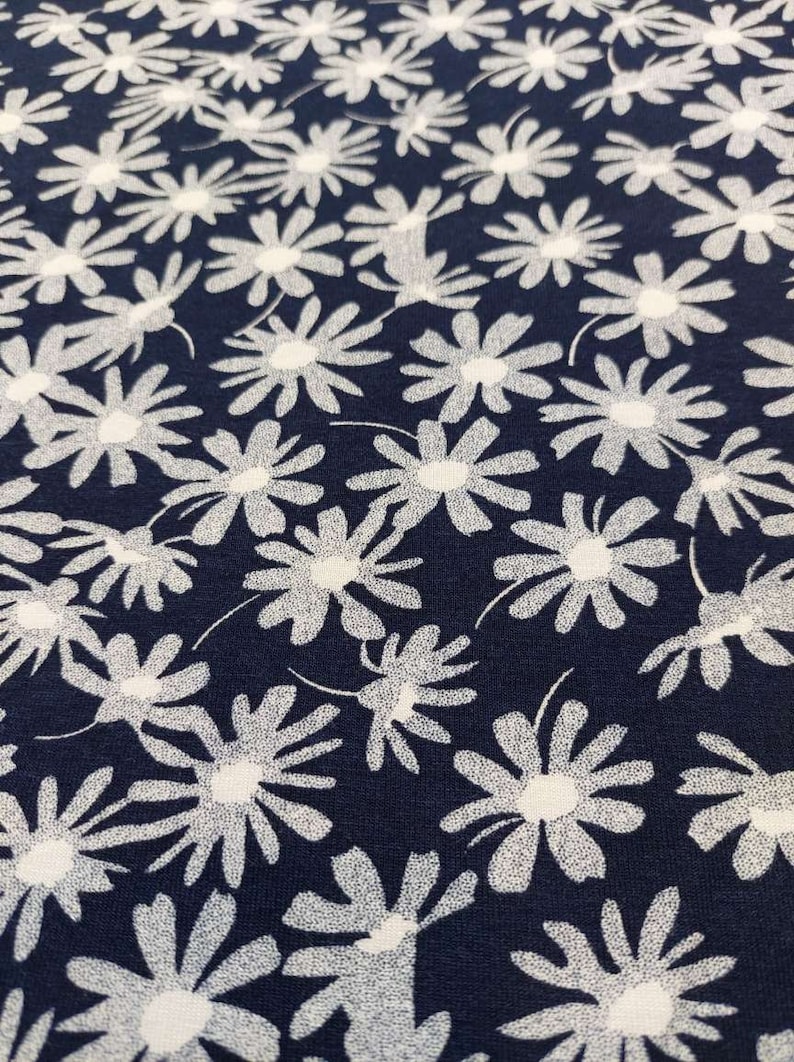 May include: A navy blue fabric with a white floral pattern. The fabric is covered in white daisy-like flowers.