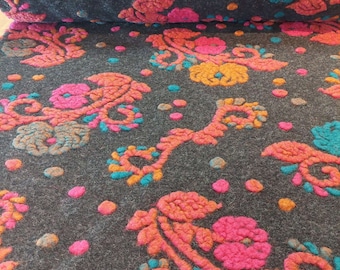 May include: Close-up of a dark grey fabric with a repeating pattern of orange, pink, and teal flowers. The fabric has a textured, fuzzy surface.
