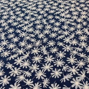 May include: A navy blue fabric with a white daisy print. The fabric is a repeating pattern of white daisies on a dark blue background.