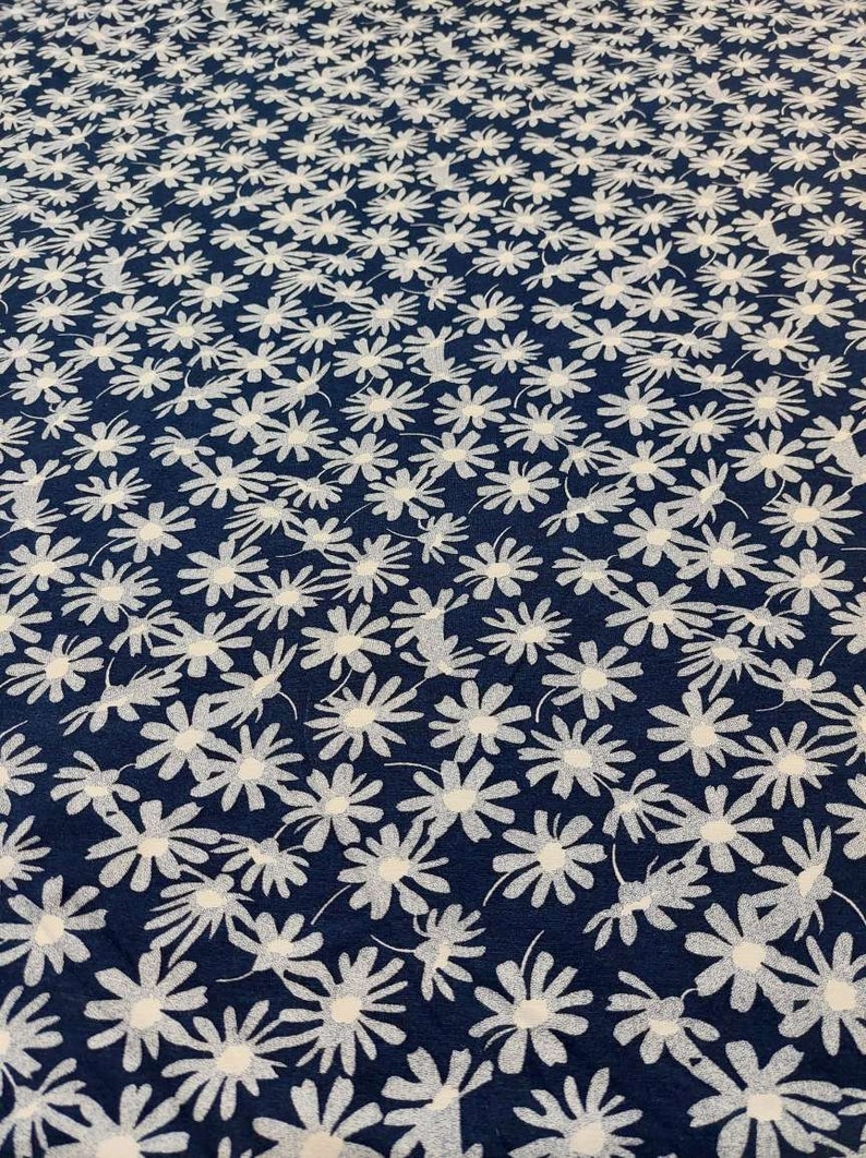 May include: A navy blue fabric with a white daisy print. The fabric is a repeating pattern of white daisies on a dark blue background.