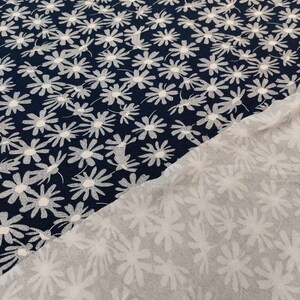 May include: Two pieces of fabric with a white daisy pattern on a navy blue background. The fabric is folded in half, showing the back side of the fabric, which is a white daisy pattern on a white background.