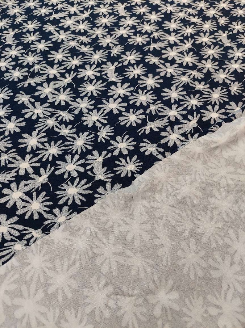 May include: Two pieces of fabric with a white daisy pattern on a navy blue background. The fabric is folded in half, showing the back side of the fabric, which is a white daisy pattern on a white background.