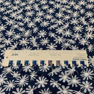 May include: Navy blue fabric with a white daisy print. The fabric is measured with a ruler that reads "Pifferi Anelio Schneidereibedarf Fermewaldstr 78 46145 Oberhausen Telefon 0208)437400 084374040 Telefax 208 Intermec www.pfende Mer infogasteri de"