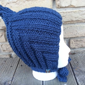 May include: A dark blue knitted hat with a pointed top and a long tie. The hat is made of a thick yarn and has a ribbed texture.