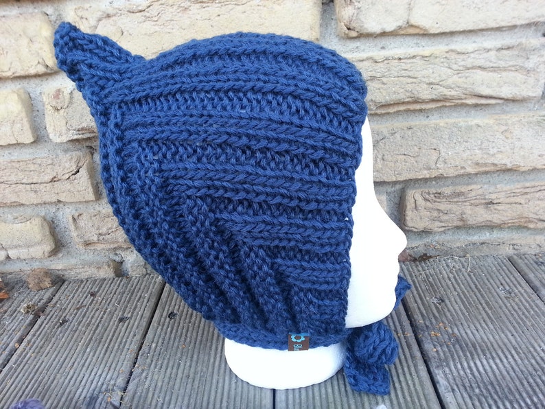 May include: A dark blue knitted hat with a pointed top and a long tie. The hat is made of a thick yarn and has a ribbed texture.