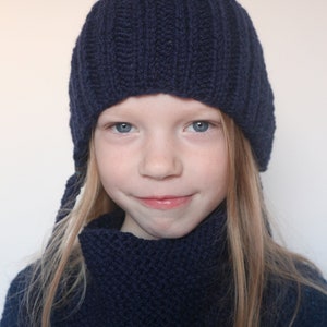 May include: A young person wearing a dark blue knitted hat and matching scarf. The hat has a pointed top and the scarf is folded around the neck.