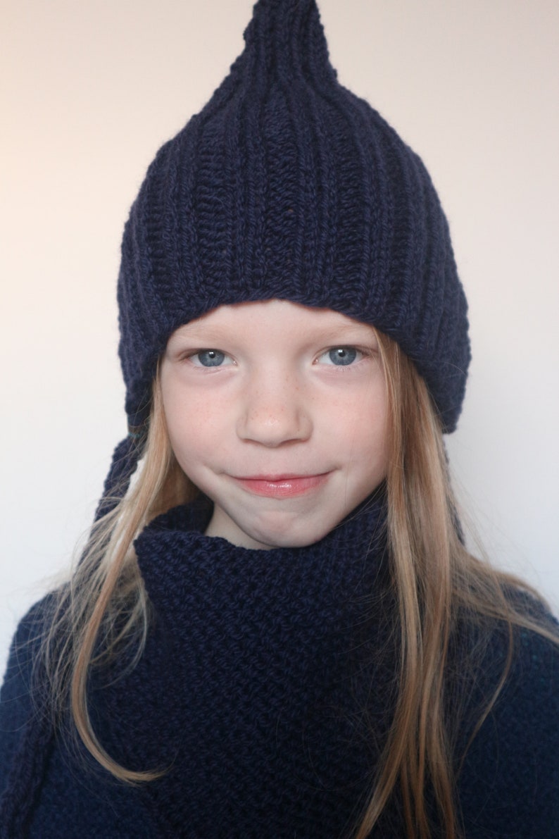May include: A young person wearing a dark blue knitted hat and matching scarf. The hat has a pointed top and the scarf is folded around the neck.