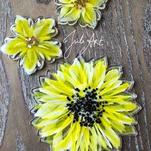 May include: Three resin coasters featuring yellow and white painted sunflowers. The largest coaster has a black glitter center. The text "July Art" is visible in the background.