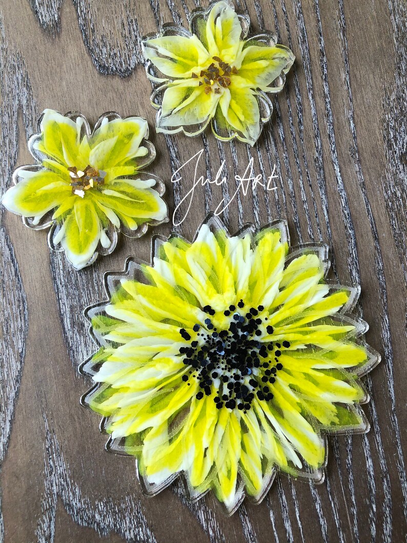 May include: Three resin coasters featuring yellow and white painted sunflowers. The largest coaster has a black glitter center. The text "July Art" is visible in the background.