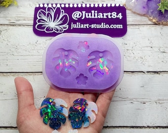 May include: Purple silicone mold with two 1.5 inch Monstera leaf earring shapes. Two finished earrings are shown in the image, one with blue and white glitter and the other with pink and blue glitter.