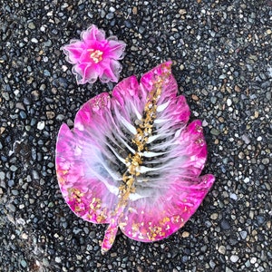 May include: Pink and white resin leaf with gold glitter, a pink flower with gold accents is in the background.