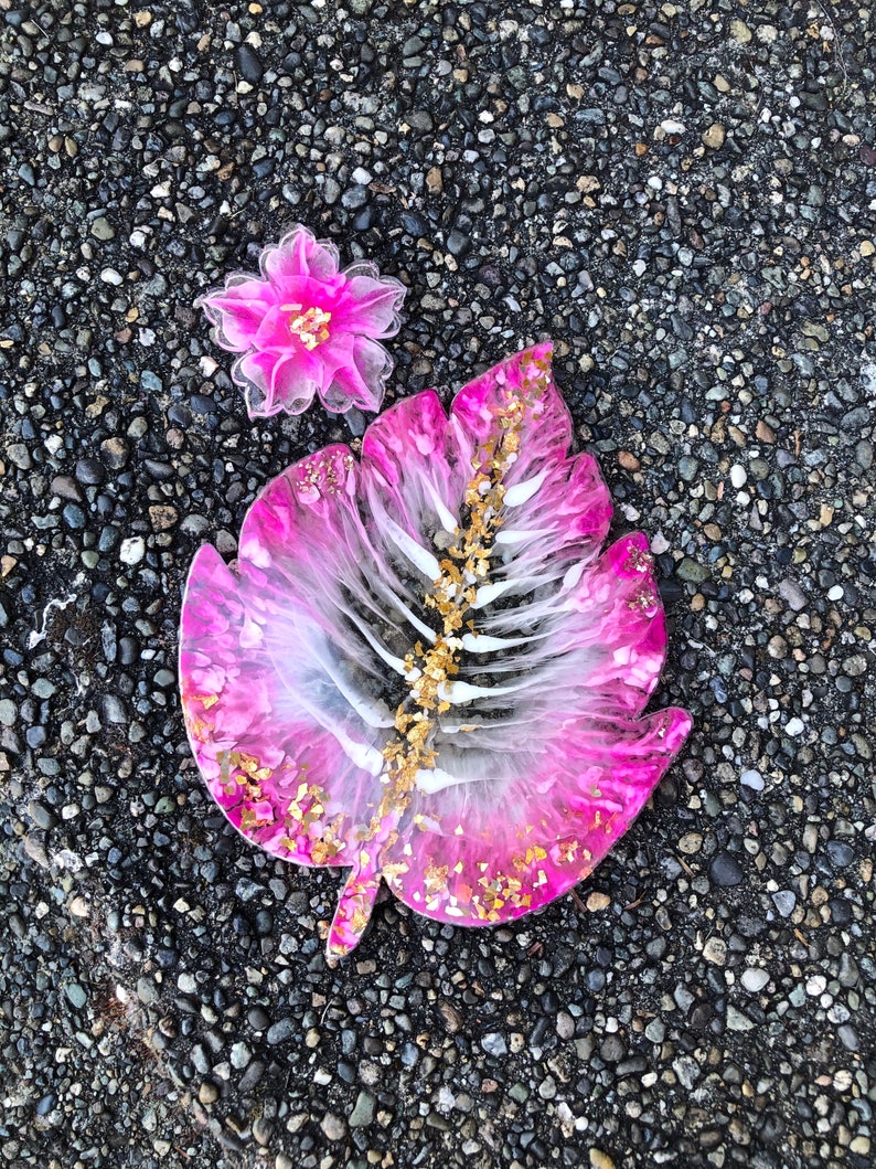 May include: Pink and white resin leaf with gold glitter, a pink flower with gold accents is in the background.