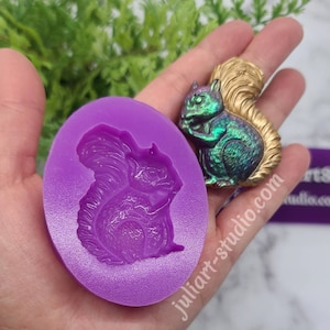 May include: Purple silicone mold with a detailed squirrel design. The mold is shown next to a finished resin squirrel with a gold tail and iridescent green body.