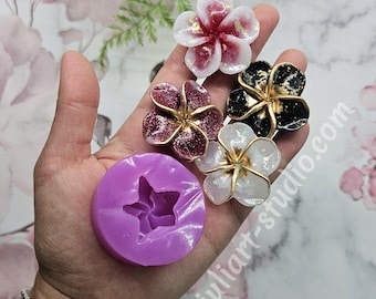 May include: A hand holds several resin flower embellishments in various colors, including white, red, black, and burgundy, with gold accents. A purple silicone flower mold is also present. The website address "juliart-studio.com" is visible.