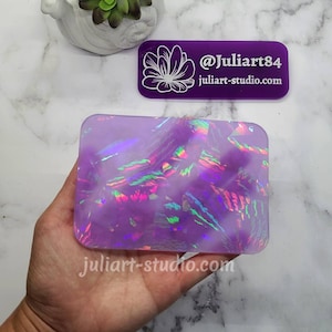 May include: A square, iridescent, purple resin coaster with a swirling pattern. The coaster is made by @juliart84 and the website is juliart-studio.com.