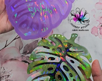 May include: Two iridescent resin monstera leaf coasters. The top coaster is purple with a holographic finish. The bottom coaster is green with a holographic finish.