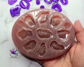 May include: A clear pink silicone mold with nine cavities shaped like small druzy slices. The mold is in a hand, and there are several purple druzy slices scattered around the mold.