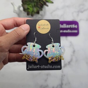 K&ouml;nnte beinhalten: Ein Paar regenbogenfarbene wei&szlig;e Kessel-Ohrringe mit goldenen Glitzerakzenten. Die Ohrringe sind handgefertigt mit Liebe und haben einen silbernen Haken.