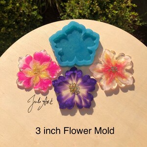 May include: A blue silicone mold shaped like a flower, with three resin flower castings in pink, purple, and yellow. The mold and castings are 3 inches in diameter. The text "3 inch Flower Mold" is written below the image.