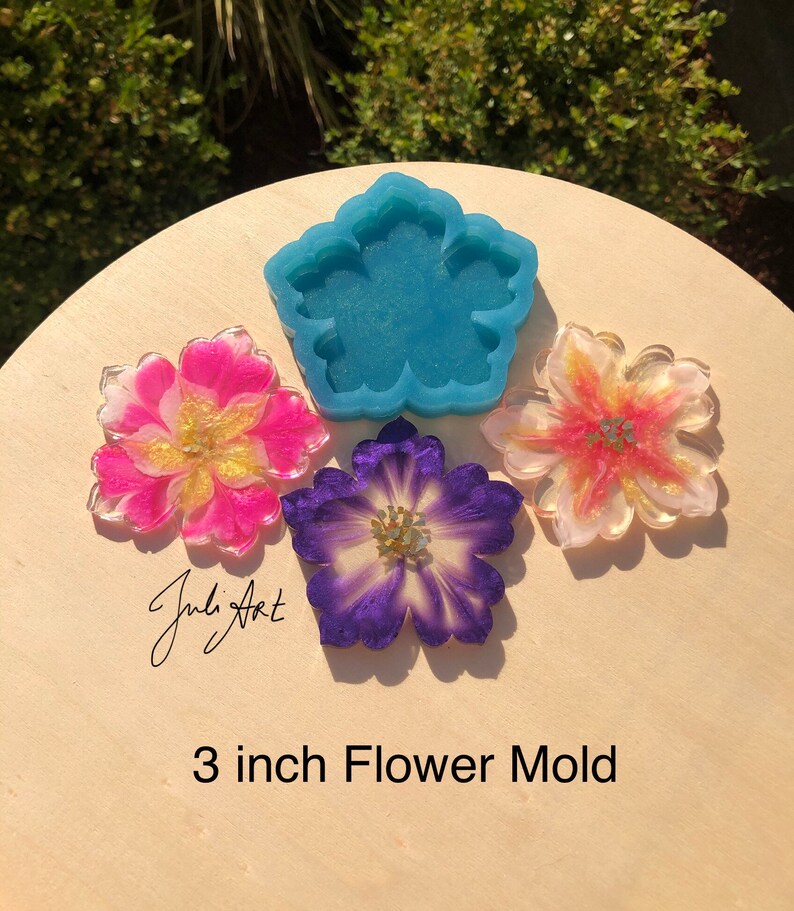 May include: A blue silicone mold shaped like a flower, with three resin flower castings in pink, purple, and yellow. The mold and castings are 3 inches in diameter. The text "3 inch Flower Mold" is written below the image.