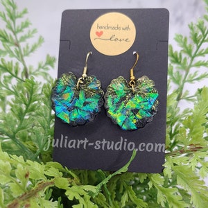 May include: A pair of iridescent green and black heart-shaped earrings with gold hooks. The earrings are handmade with love and are displayed on a black card with the text "handmade with love".