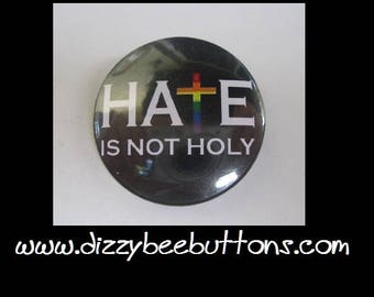 May include: A black button with a white cross and the text "HATE IS NOT HOLY". The cross is rainbow colored.