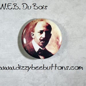 May include: A button featuring a sepia-toned portrait of W.E.B. Du Bois, a prominent African American civil rights activist and scholar. The button is round and has a glossy finish.