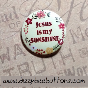 May include: A round button with a cream background and a floral border. The text "Jesus is my sunshine" is written in red on the button.