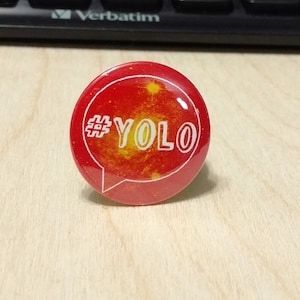 May include: A red and yellow round button with a white speech bubble and the text "#YOLO" inside.