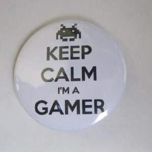 May include: White button with black text that reads "Keep Calm I'm a Gamer" with a pixelated spaceship graphic above the text.
