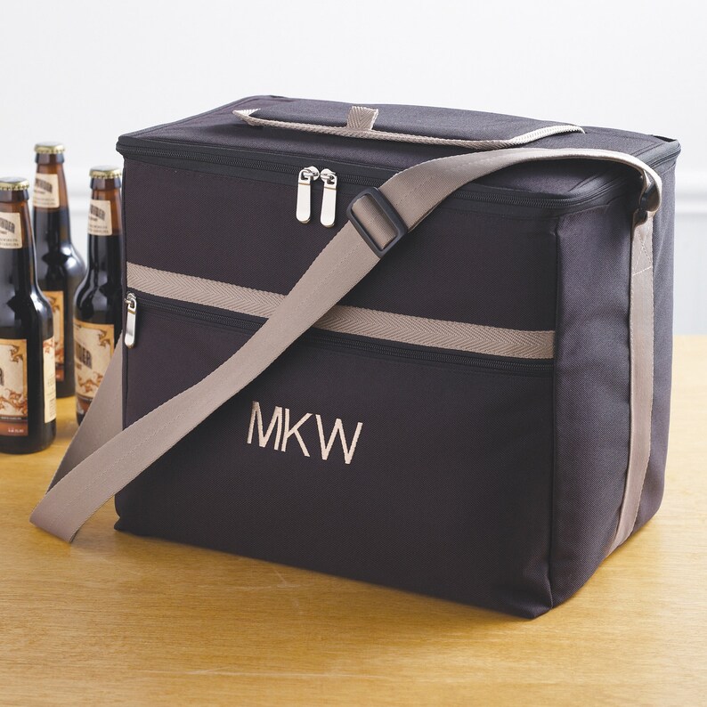 May include: Black insulated cooler bag with a tan adjustable shoulder strap and zipper closure. The bag has a tan stripe and the initials "MKW" embroidered on the front.