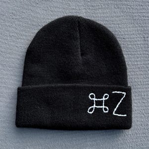 May include: Black knit beanie with a folded brim. The beanie features white embroidered letters "HZ" on the front. The hat is made of a soft, knitted material and is suitable for cold weather.
