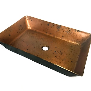 May include: A rectangular copper sink with a hammered finish and a drain hole in the center. The sink has a dark brown rim.