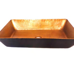 May include: A rectangular copper sink with a hammered finish. The sink has a black exterior and a gold interior.